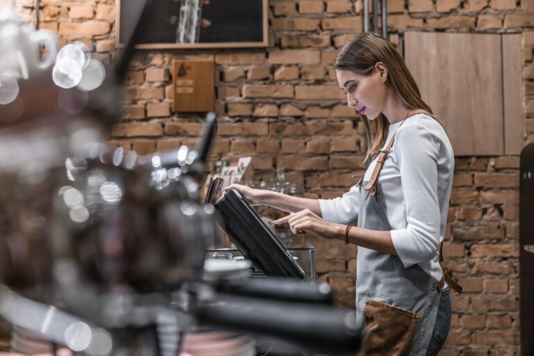 Young woman at counter with cashbox working in coffee shop
